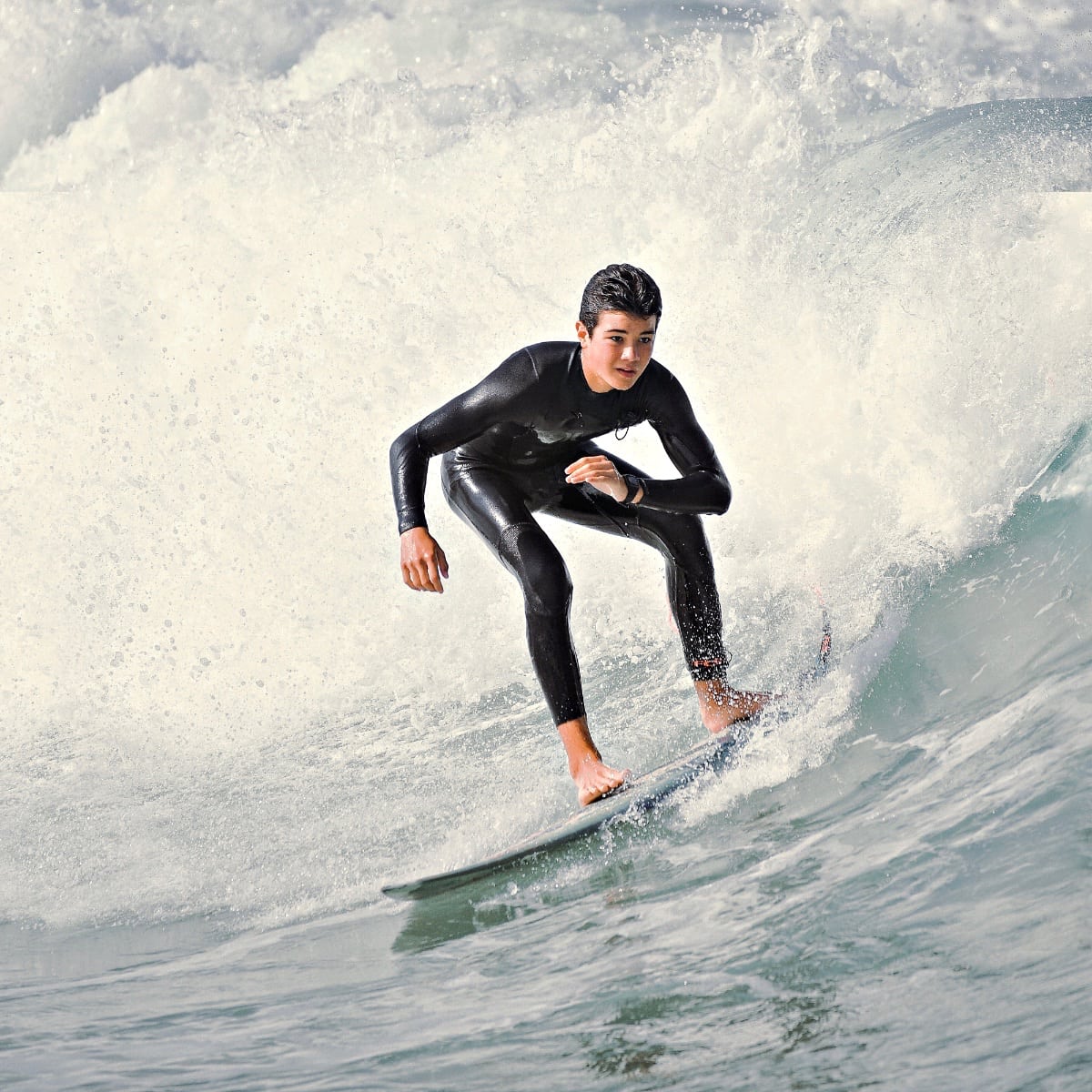 Un adolescent en combinaison noire surfe sur une grosse vague au cours d’un surfari.
