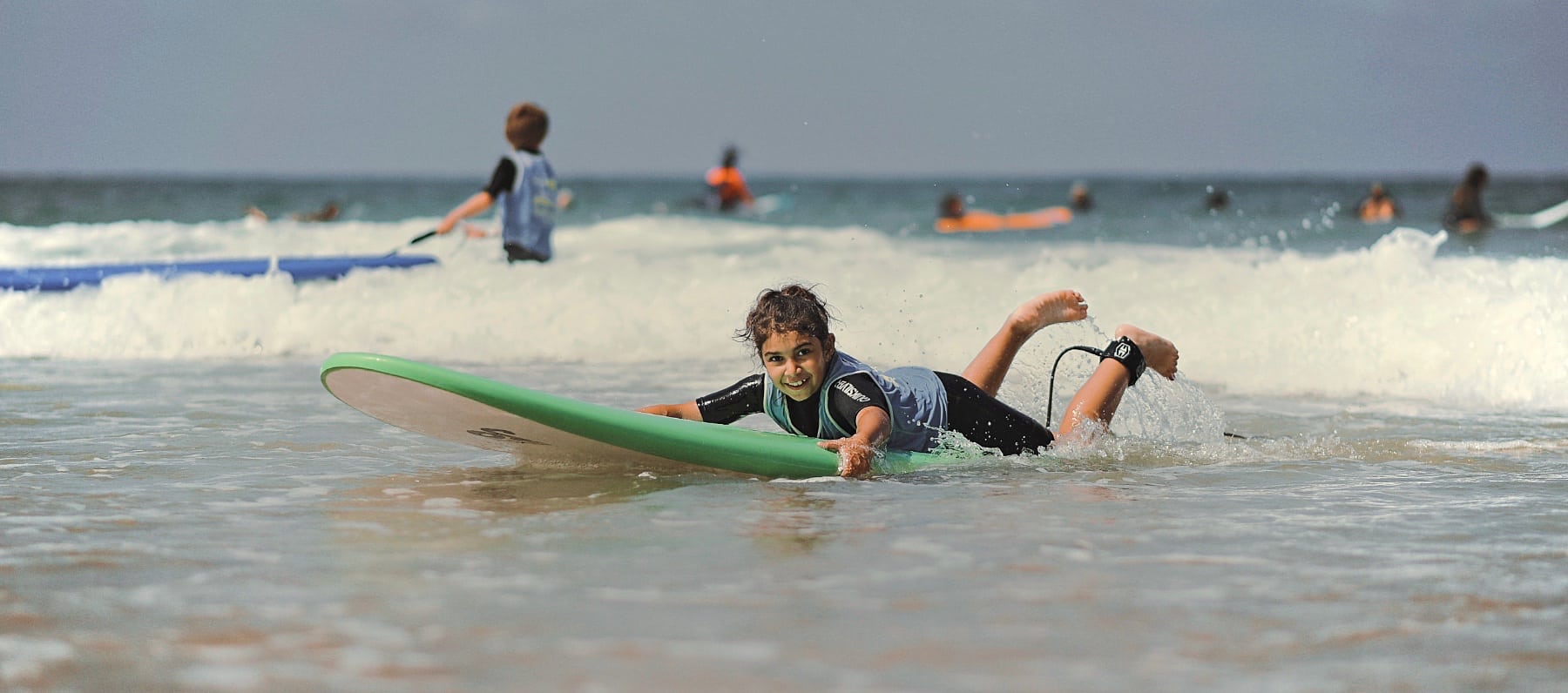 Une fille fait du surf allongée sur sa planche à Capbreton, et regarde en direction de la caméra.