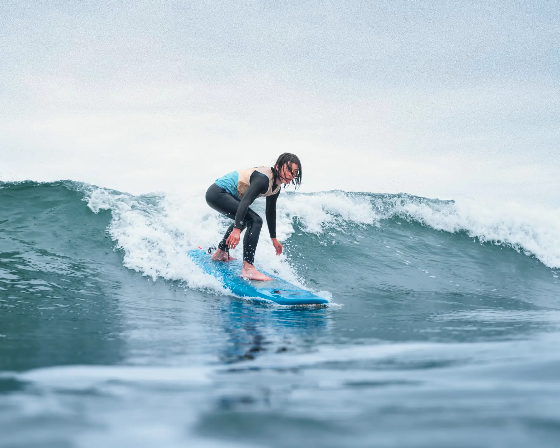 Un adolescent sur une planche de surf bleue, concentré, en train de prendre une vague