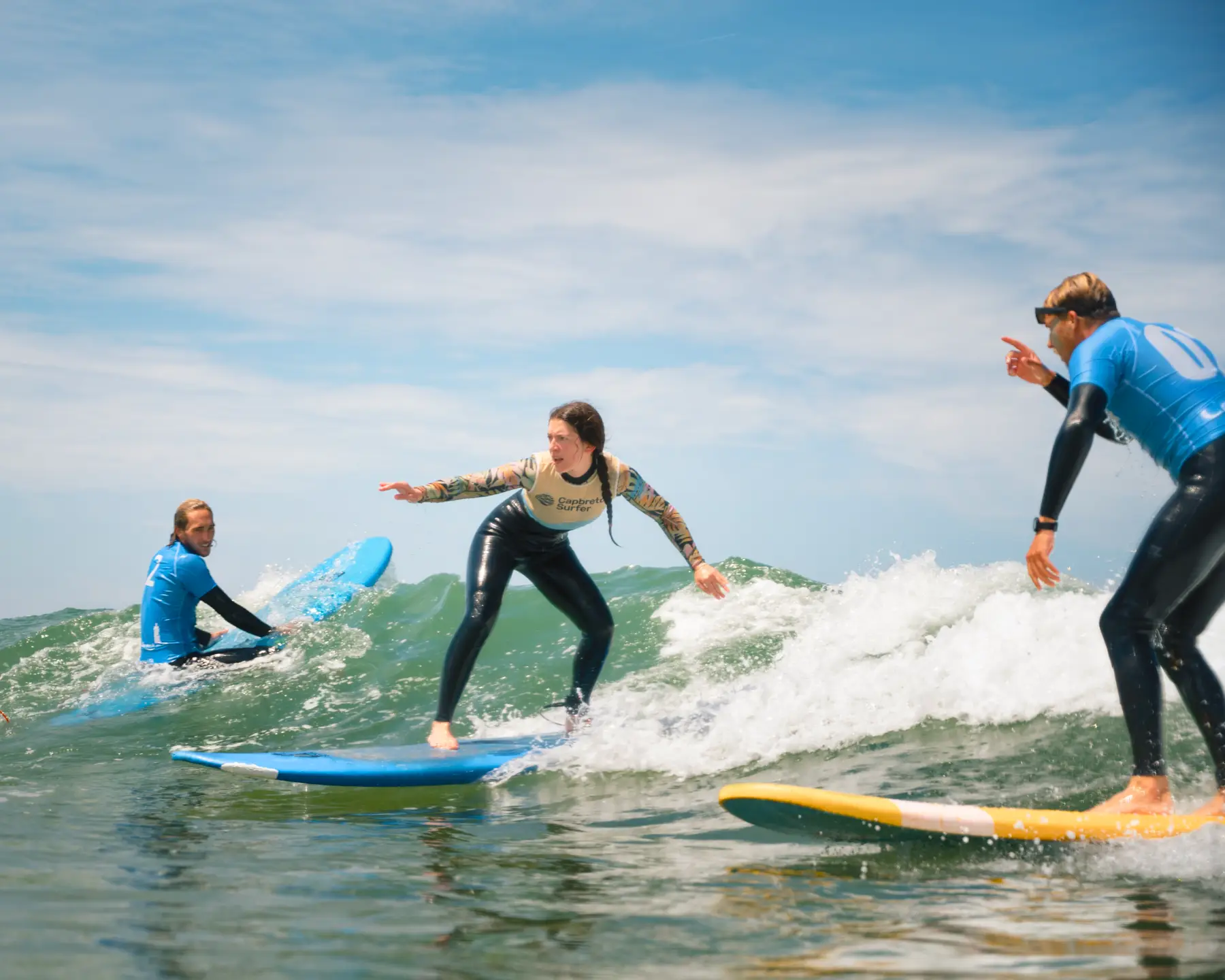 Un groupe de surfeurs en action sur des vagues, avec une élève adulte recevant des conseils en temps réel de la part des moniteurs