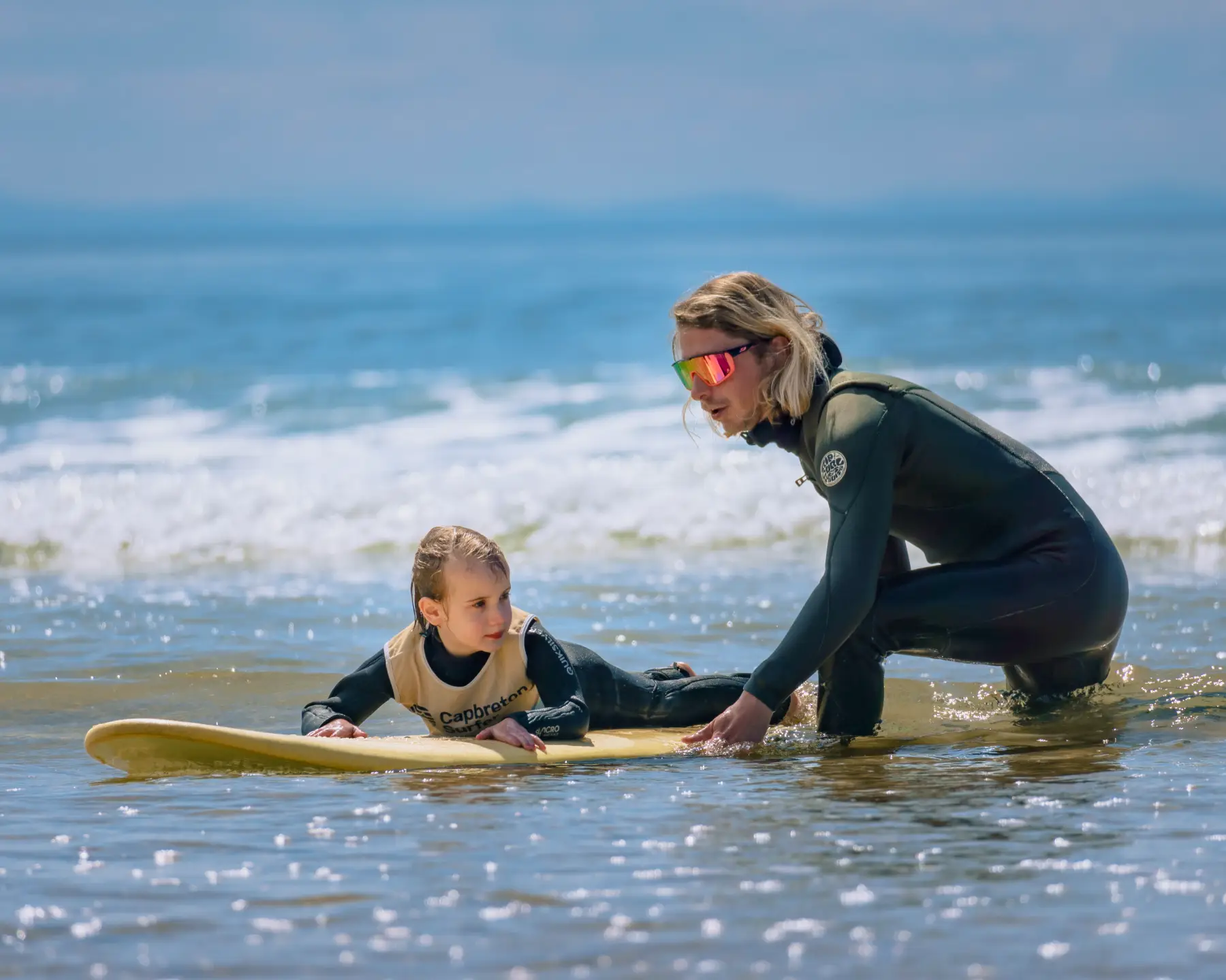 Un moniteur aidant un jeune enfant sur une planche de surf dans des eaux peu profondes
