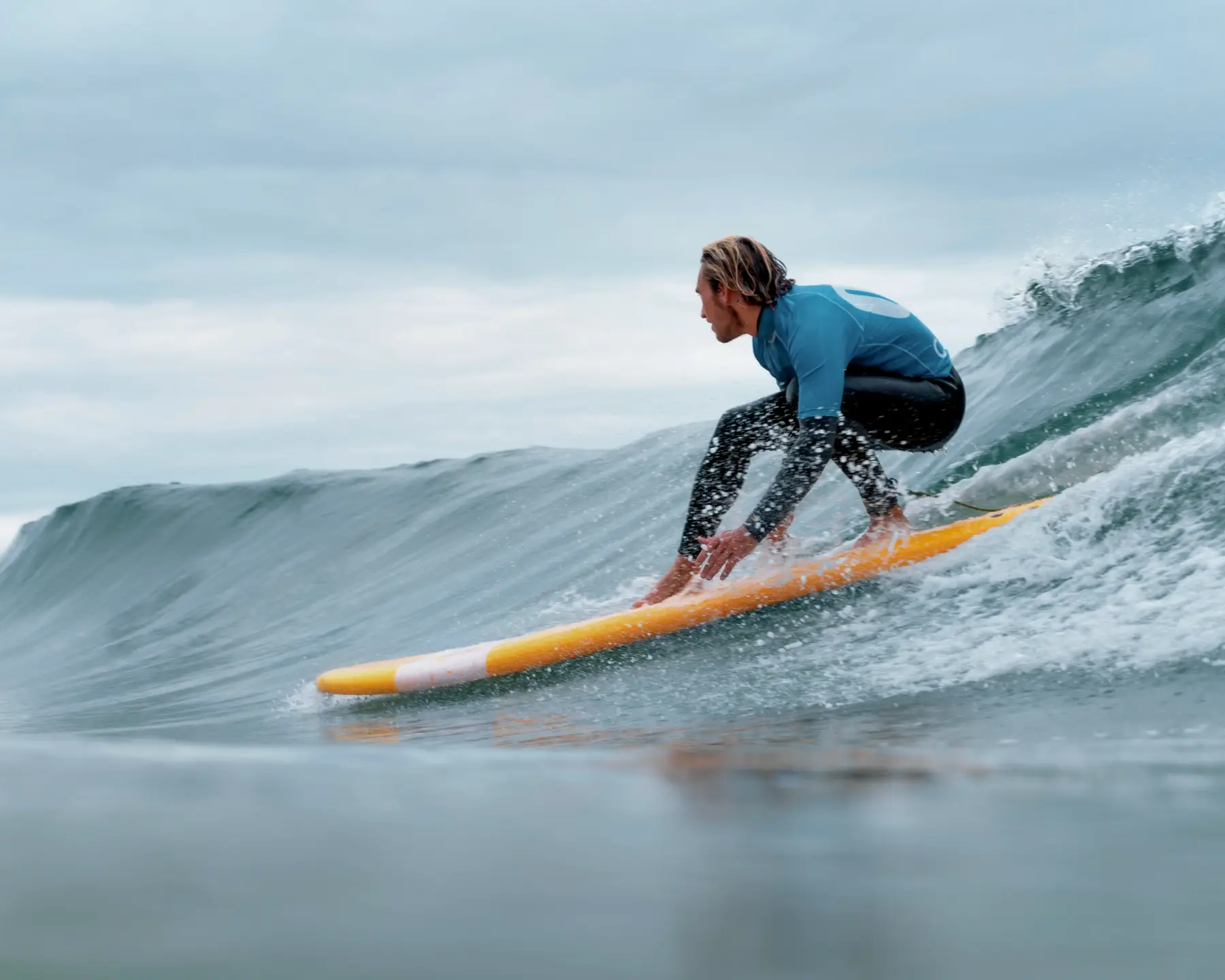 Un surfeur concentré, en combinaison noire et bleue, exécutant une manœuvre sur une vague
